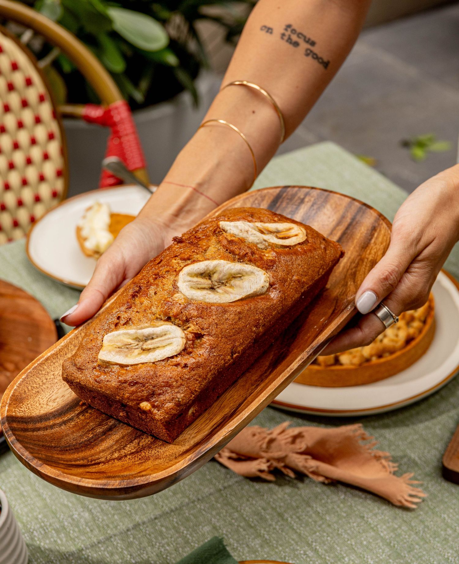 Freshly baked banana bread with sliced bananas on top served on a wooden platter.