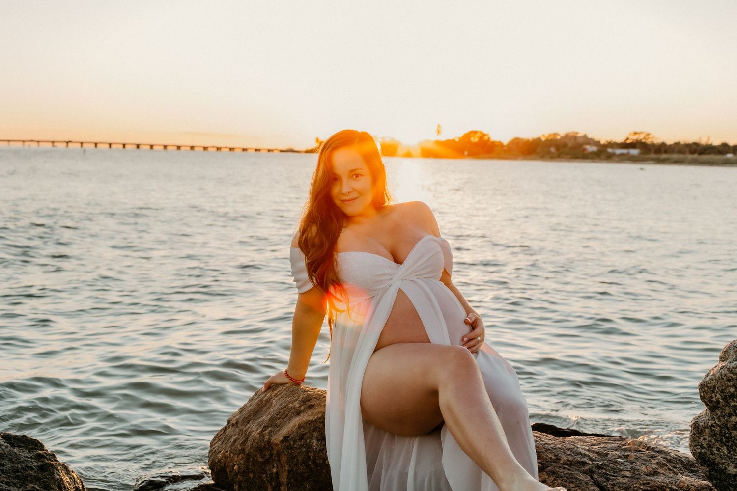 Sunset maternity portrait on coastal rocks with warm golden light and ocean views.