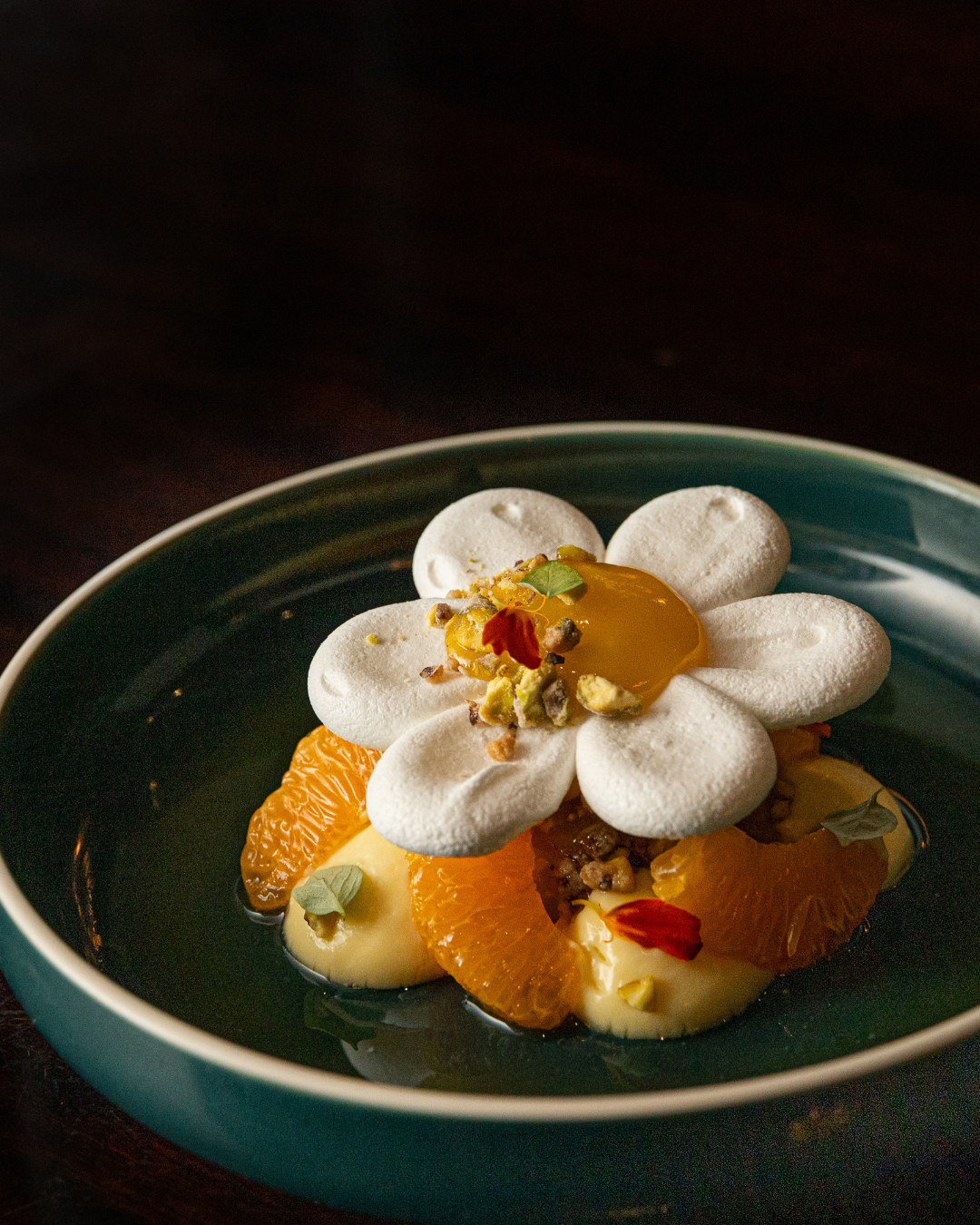 Elegant dessert with whipped cream rosettes and orange segments on a turquoise plate.