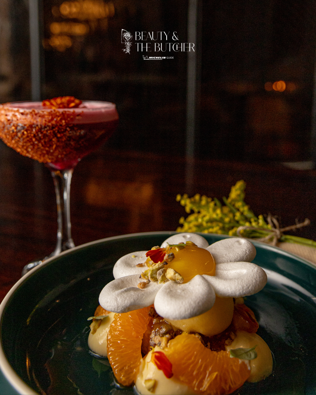 Artistically plated citrus dessert with whipped cream and garnishes on a dark plate in moody lighting.