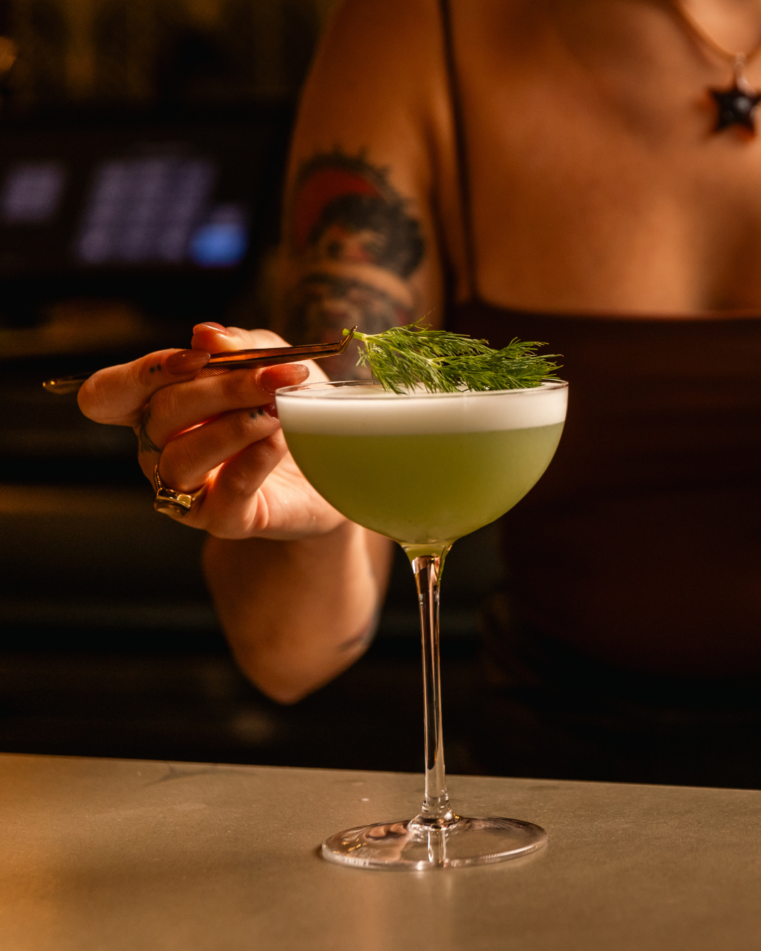 Elegant green cocktail served in a coupe glass with garnish on a dark bar counter.