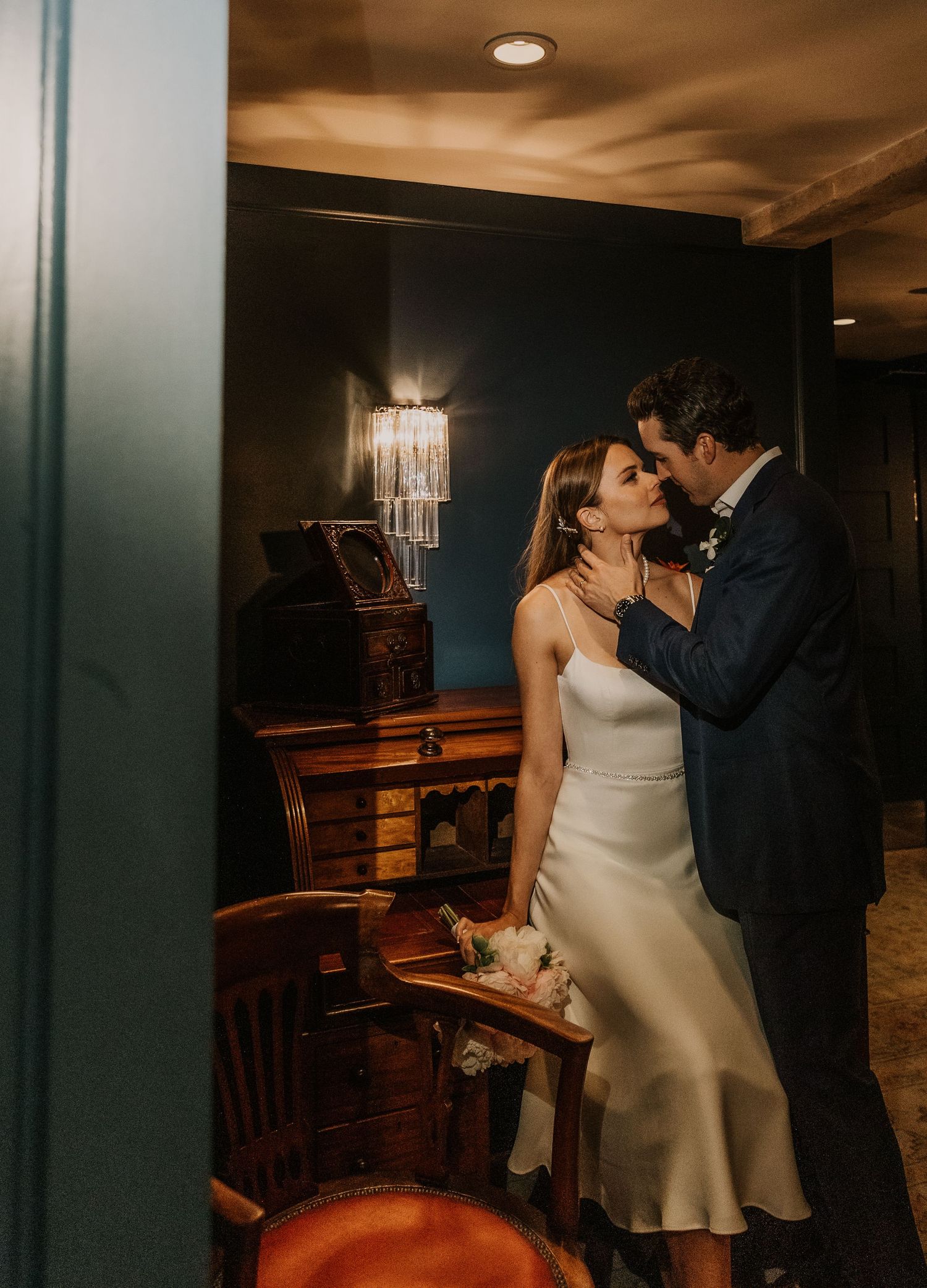 Romantic couple sharing intimate moment in dimly lit room with chandelier.