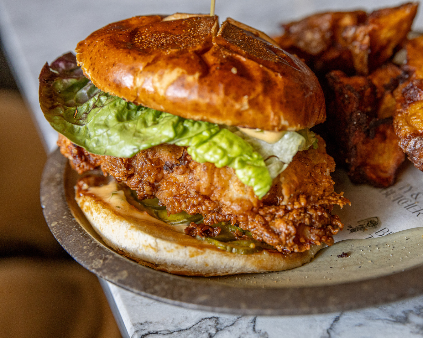 Crispy chicken sandwiches with lettuce on toasted buns against marble background.
