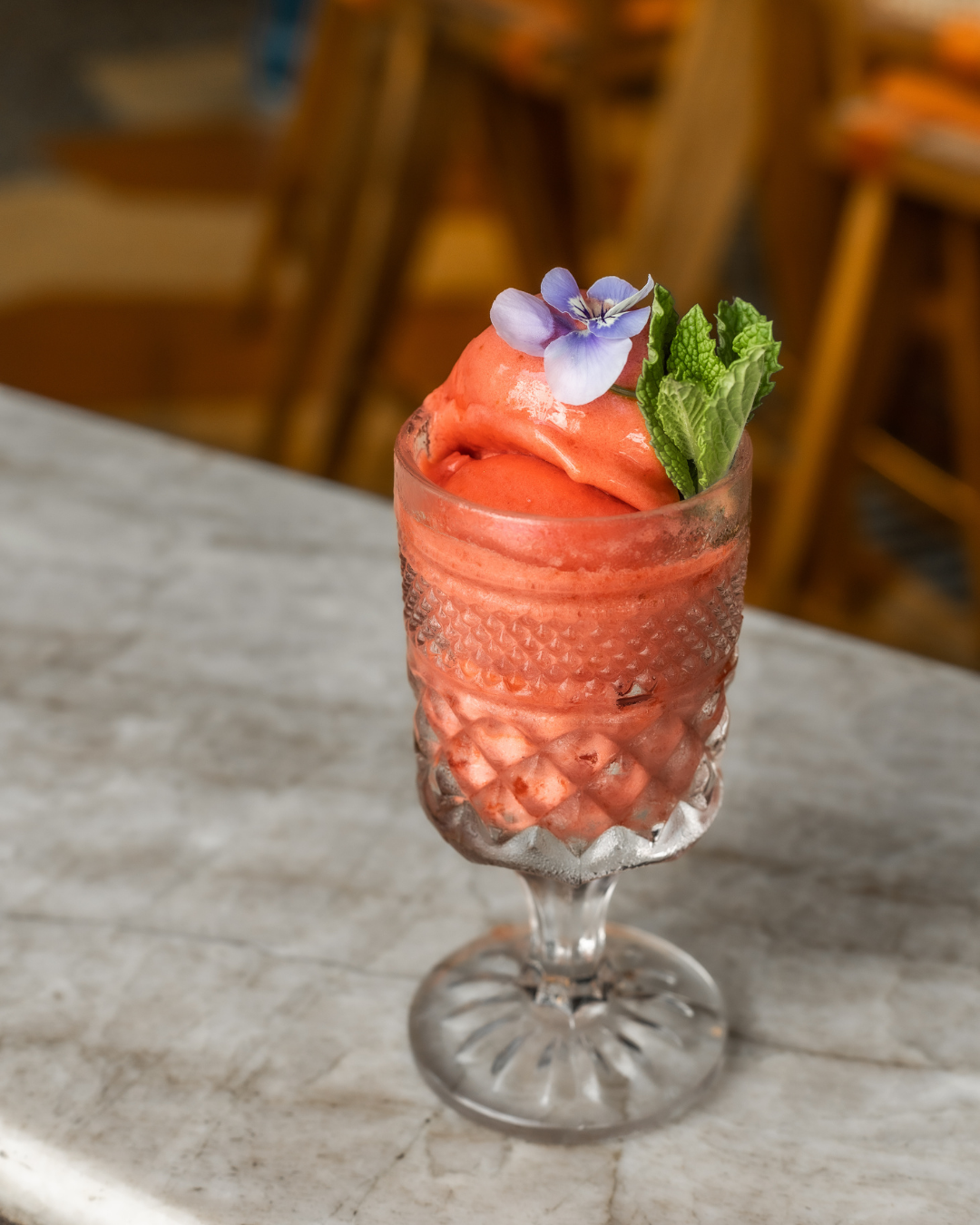 Frozen strawberry cocktail in vintage glass with mint and edible flower garnish.