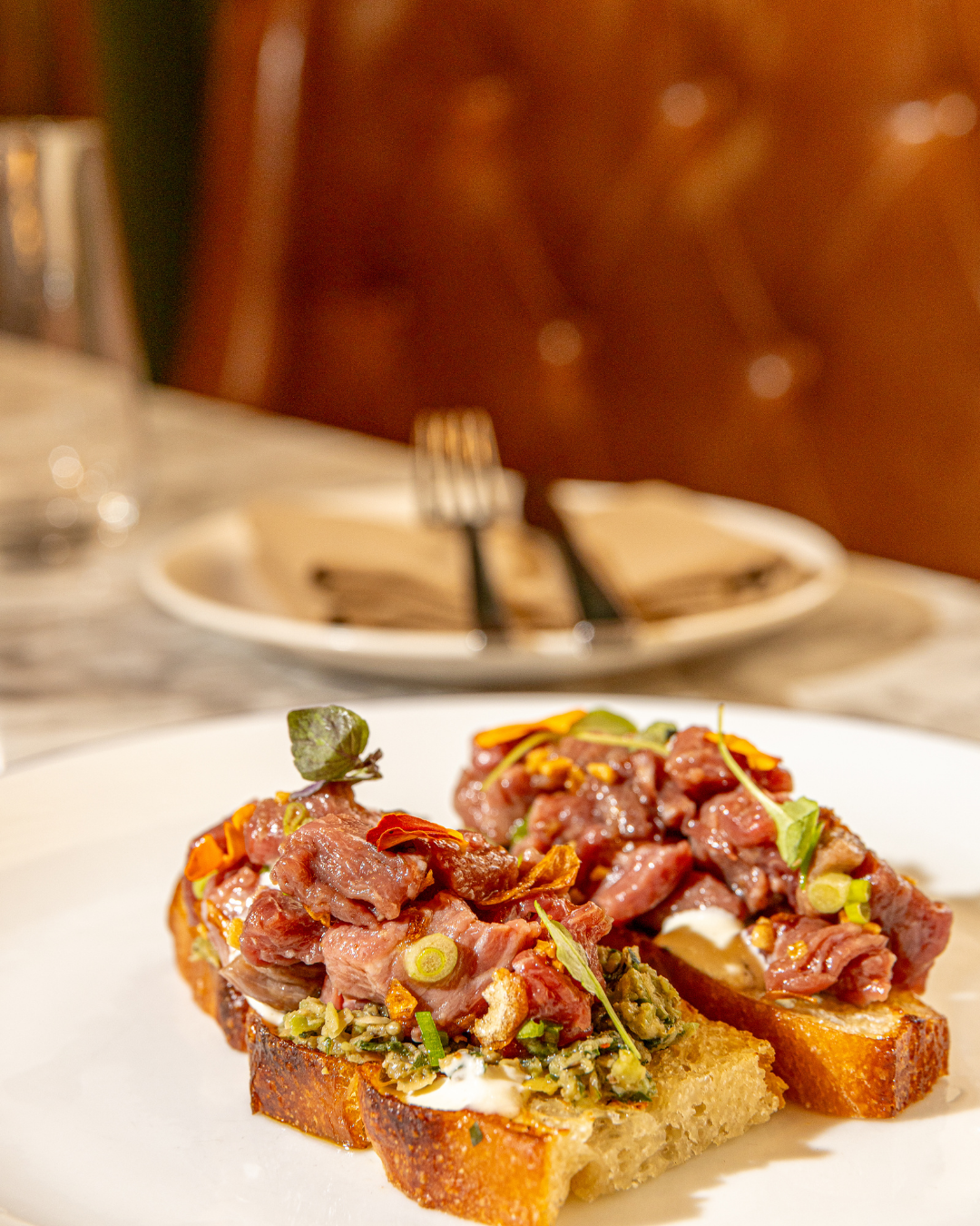 Bruschetta topped with rare meat and microgreens on rustic bread.