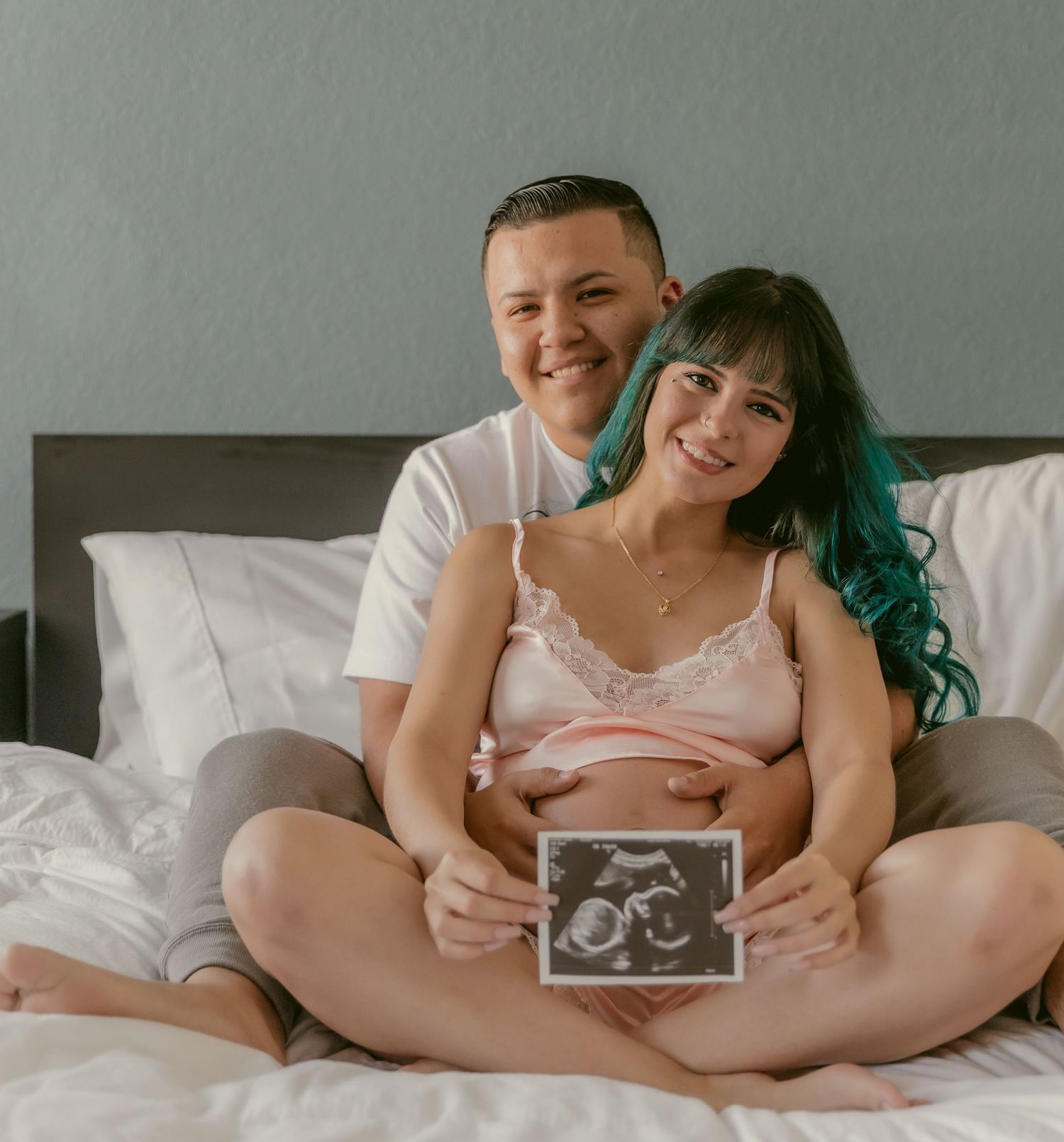 Intimate indoor photoshoot with ultrasound photos on a white bed.