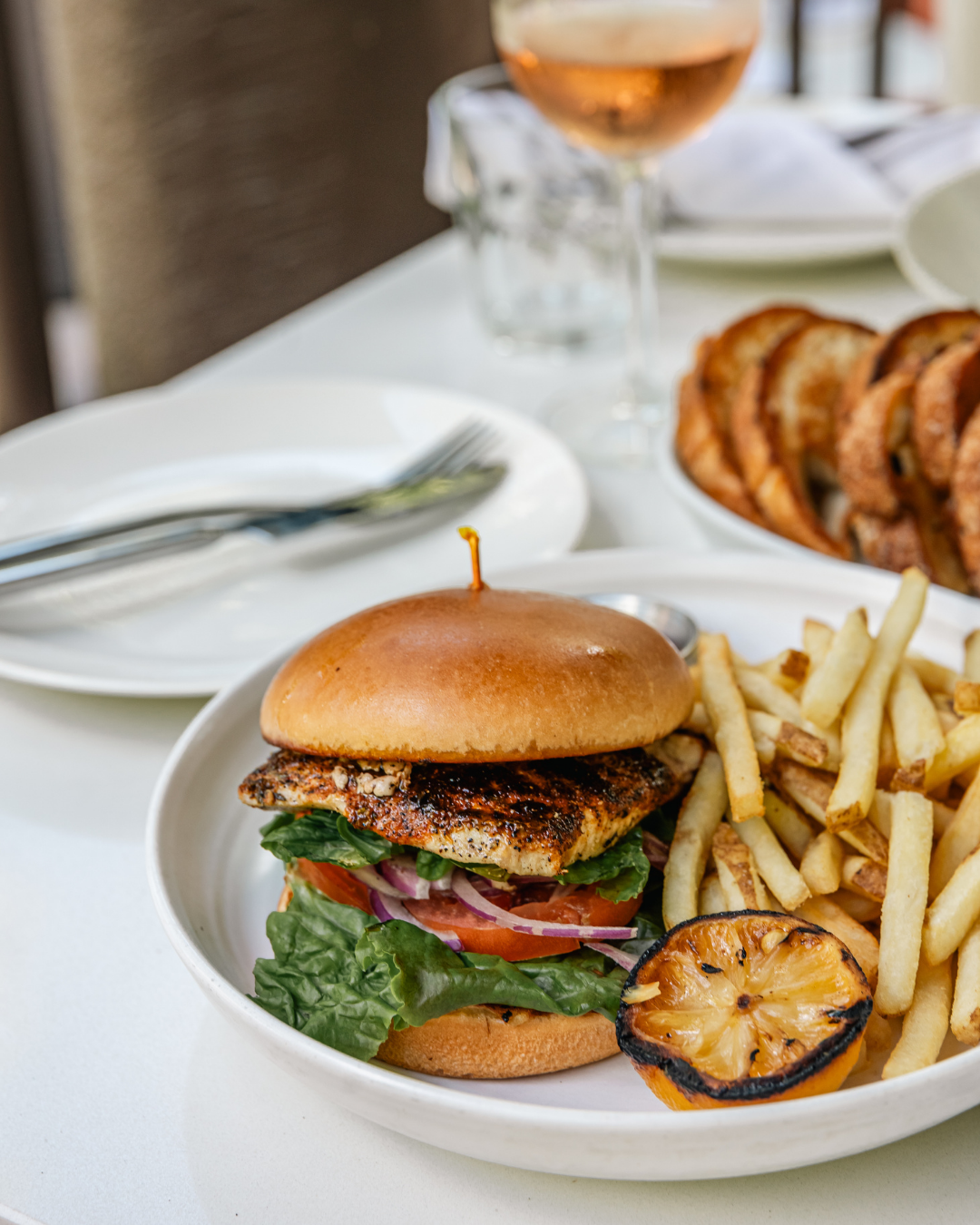 Grilled burger with lettuce and tomato served alongside crispy french fries on white plate.
