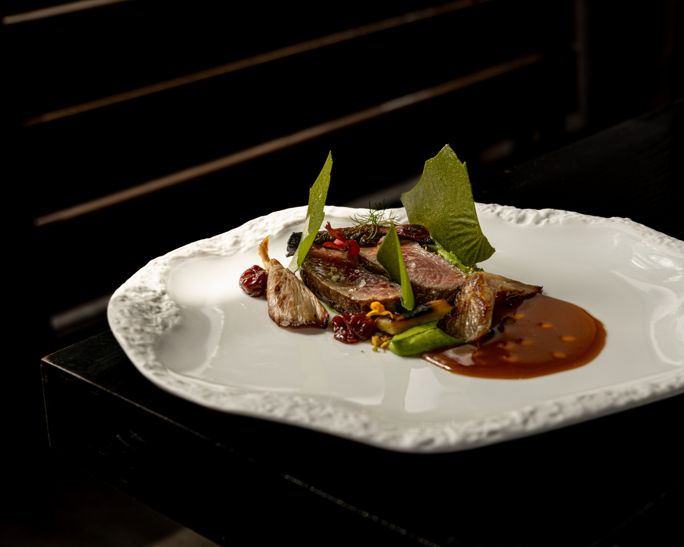 Elegantly plated fine dining dishes on white plates with dramatic lighting.