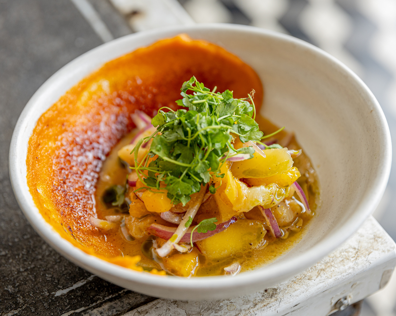 Artfully plated fine dining dish garnished with fresh herbs in an orange-hued sauce.