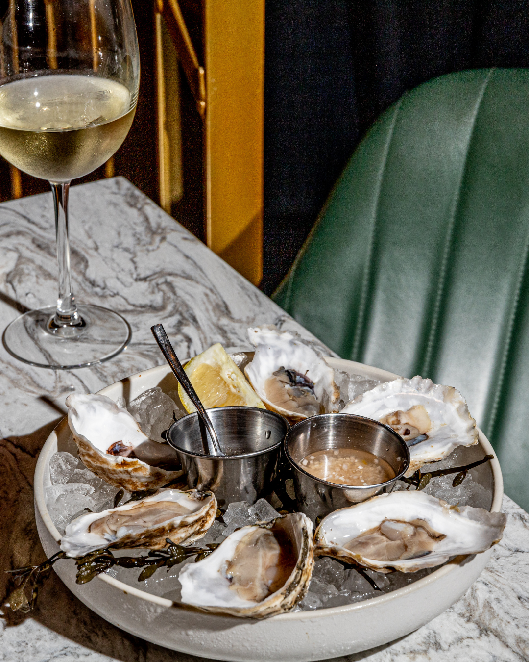 Fresh oysters on ice served with wine and condiments on a marble table surface.