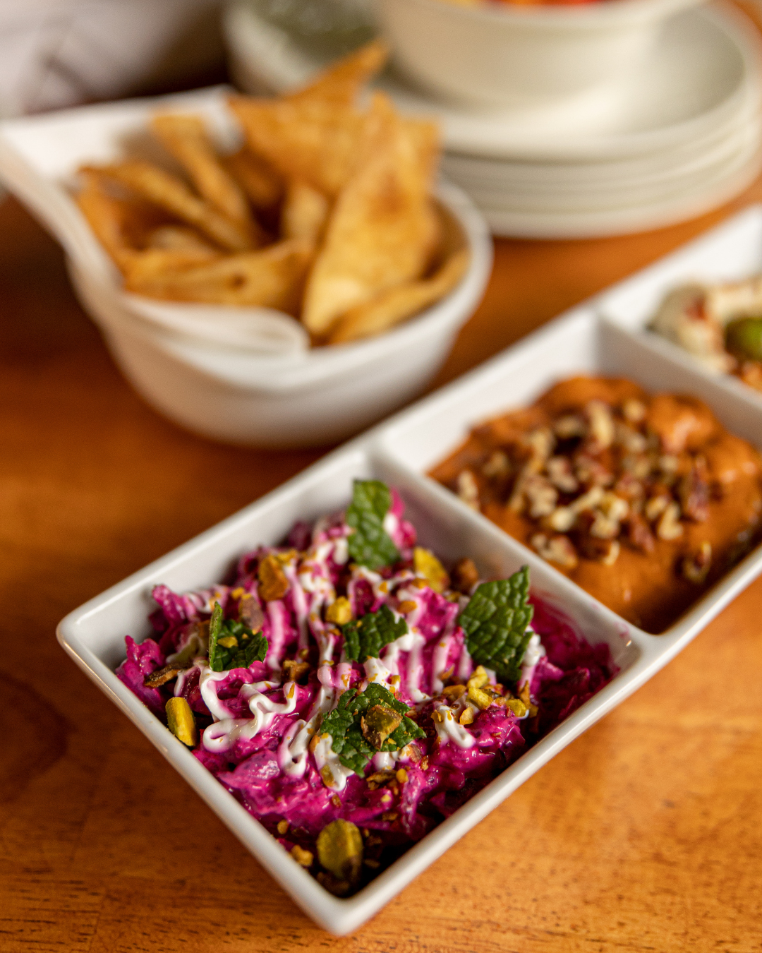 Colorful appetizer spread featuring vibrant beet salad, tortilla chips and dips in white ceramic dishes.