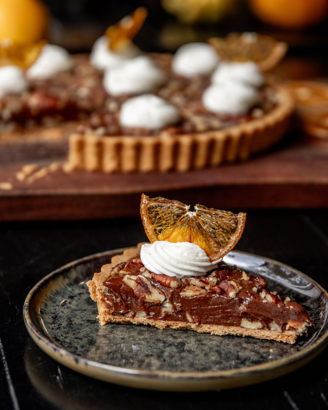 Slices of decadent chocolate tart topped with whipped cream on dark plates.