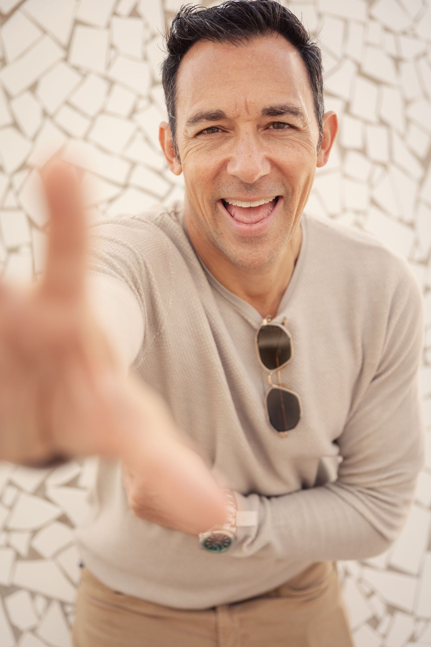 Person in a light sweater smiles warmly while sitting against a textured stone wall background.