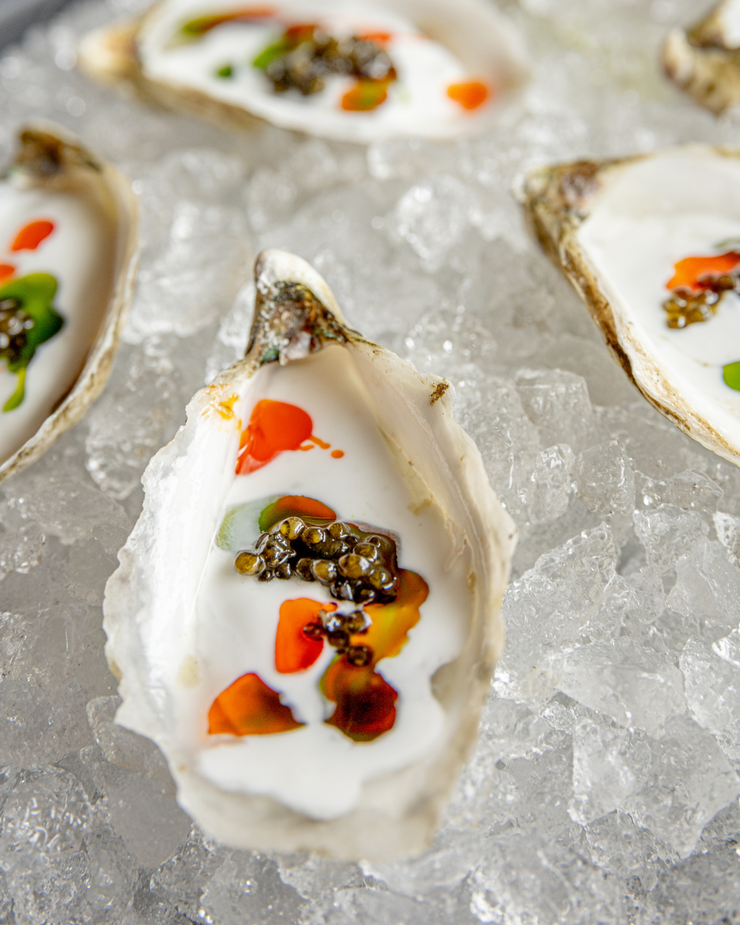 Fresh oysters on ice garnished with colorful sauces and herbs.