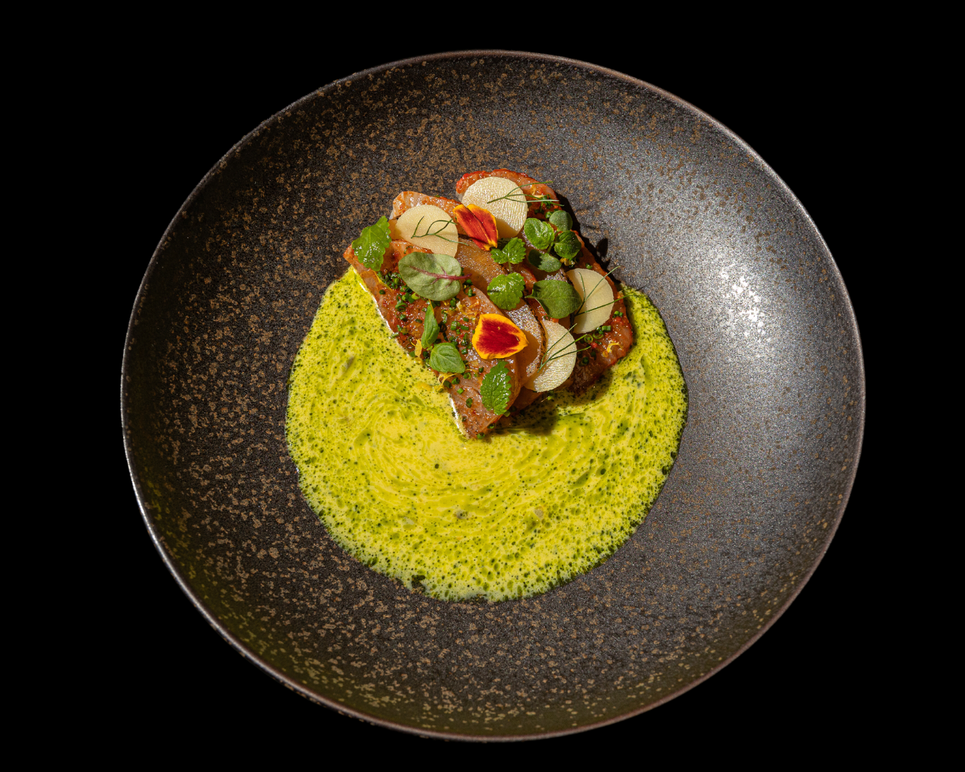 Modern plated dish featuring yellow saffron rice and protein on a dark ceramic plate.
