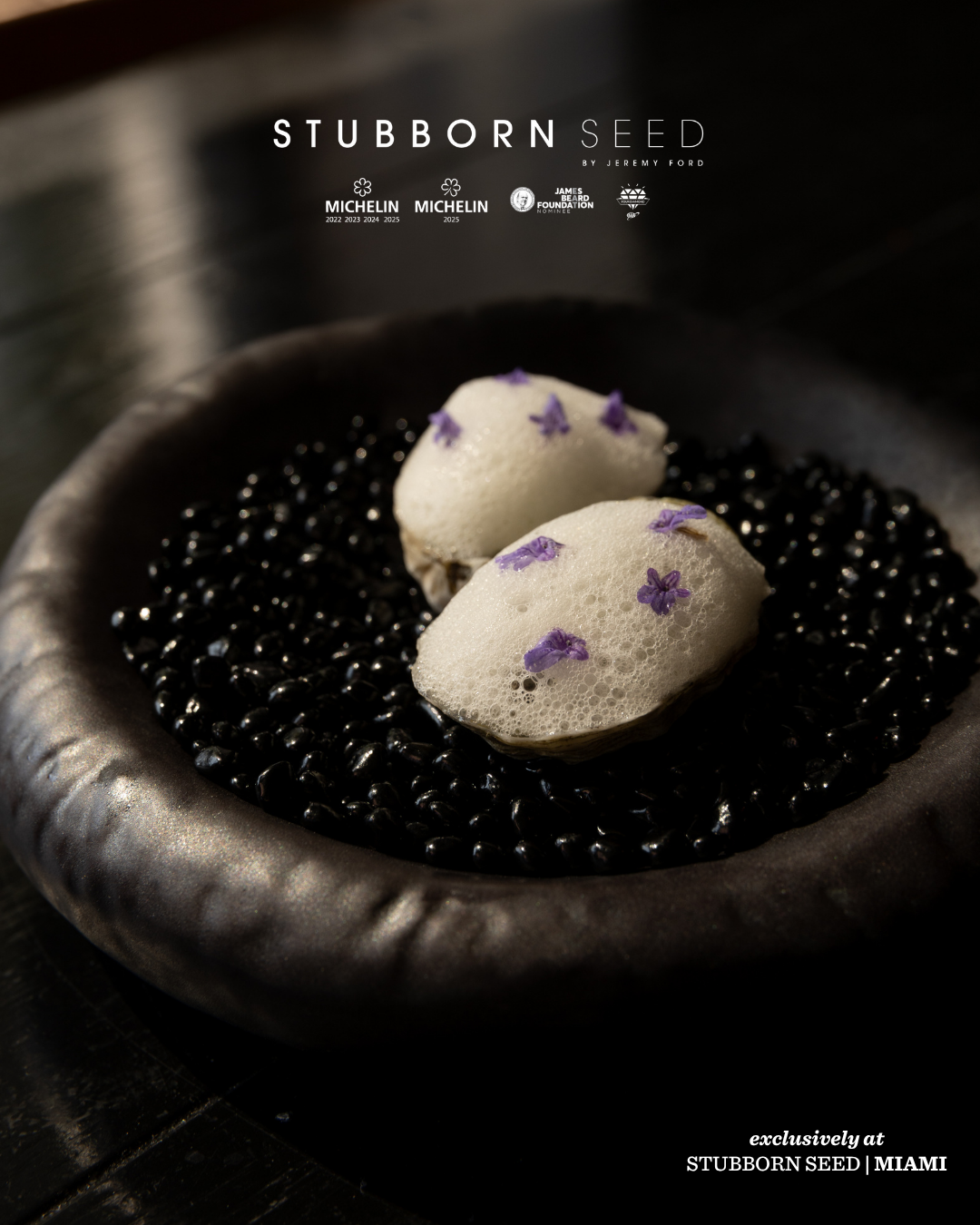 Minimalist plated white meringues with purple flower garnish on black caviar presentation.