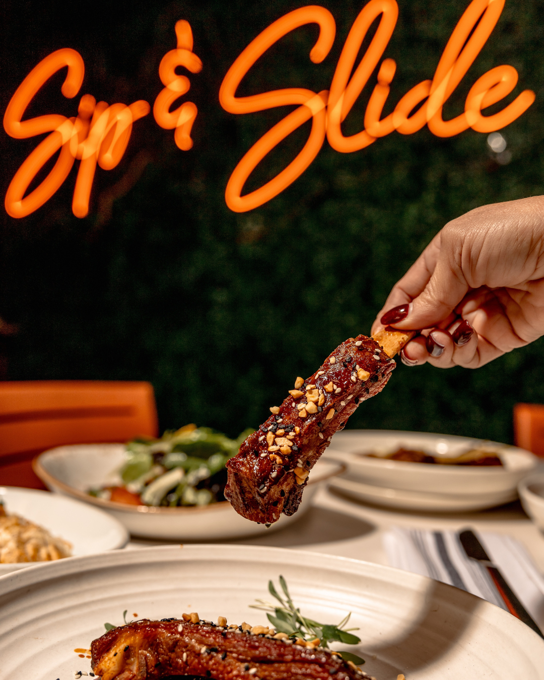 Glazed ribs being served on white plates with dramatic lighting and orange text overlay.