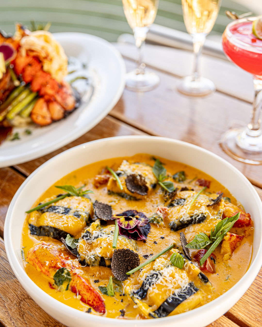 Elegant seafood curry with black rolls and herbs served alongside cocktails.