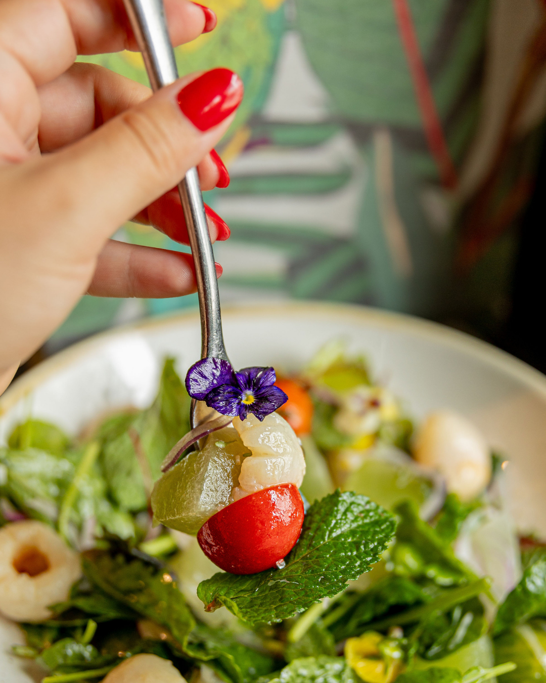 Fork lifting fresh salad ingredients with edible purple flower garnish.