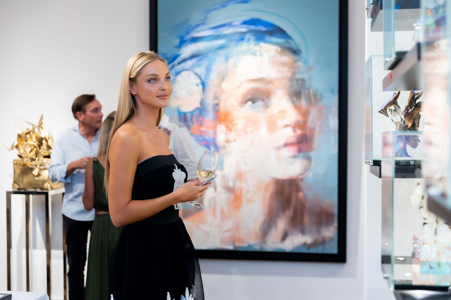Couple interacting in modern art gallery with blue artwork and gold sculptures visible.