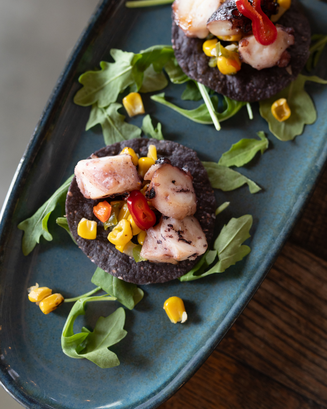 Elegant appetizers with seafood and microgreens plated on a dark ceramic dish.