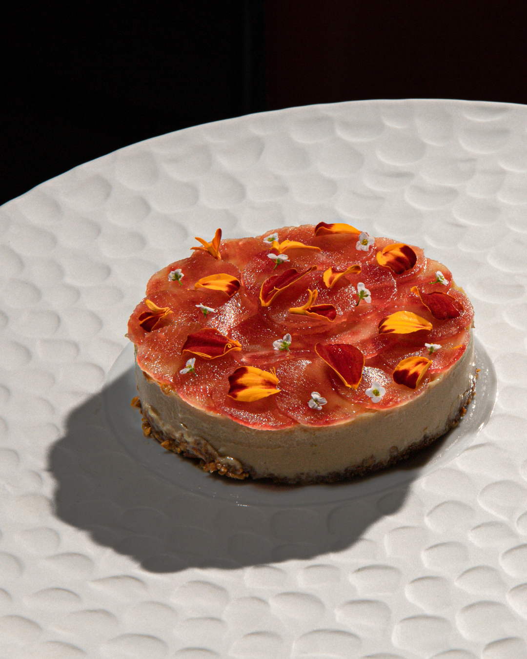 Elegant dessert featuring a pink jelly-topped cheesecake on a textured white plate.