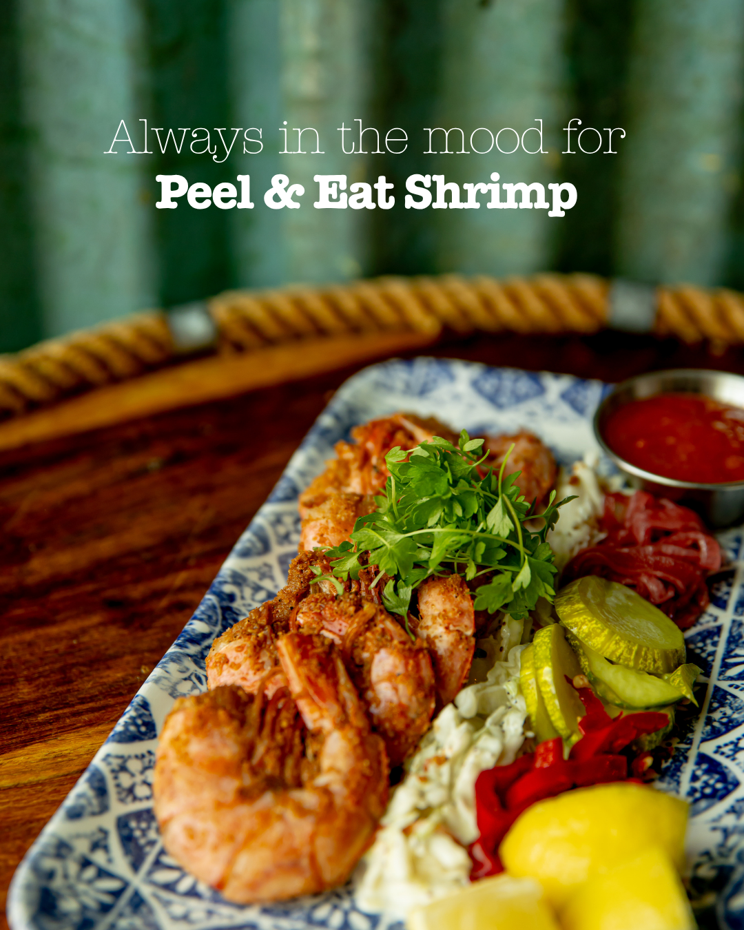 Peel and eat shrimp served with lemon and cocktail sauce on decorative blue and white plate.