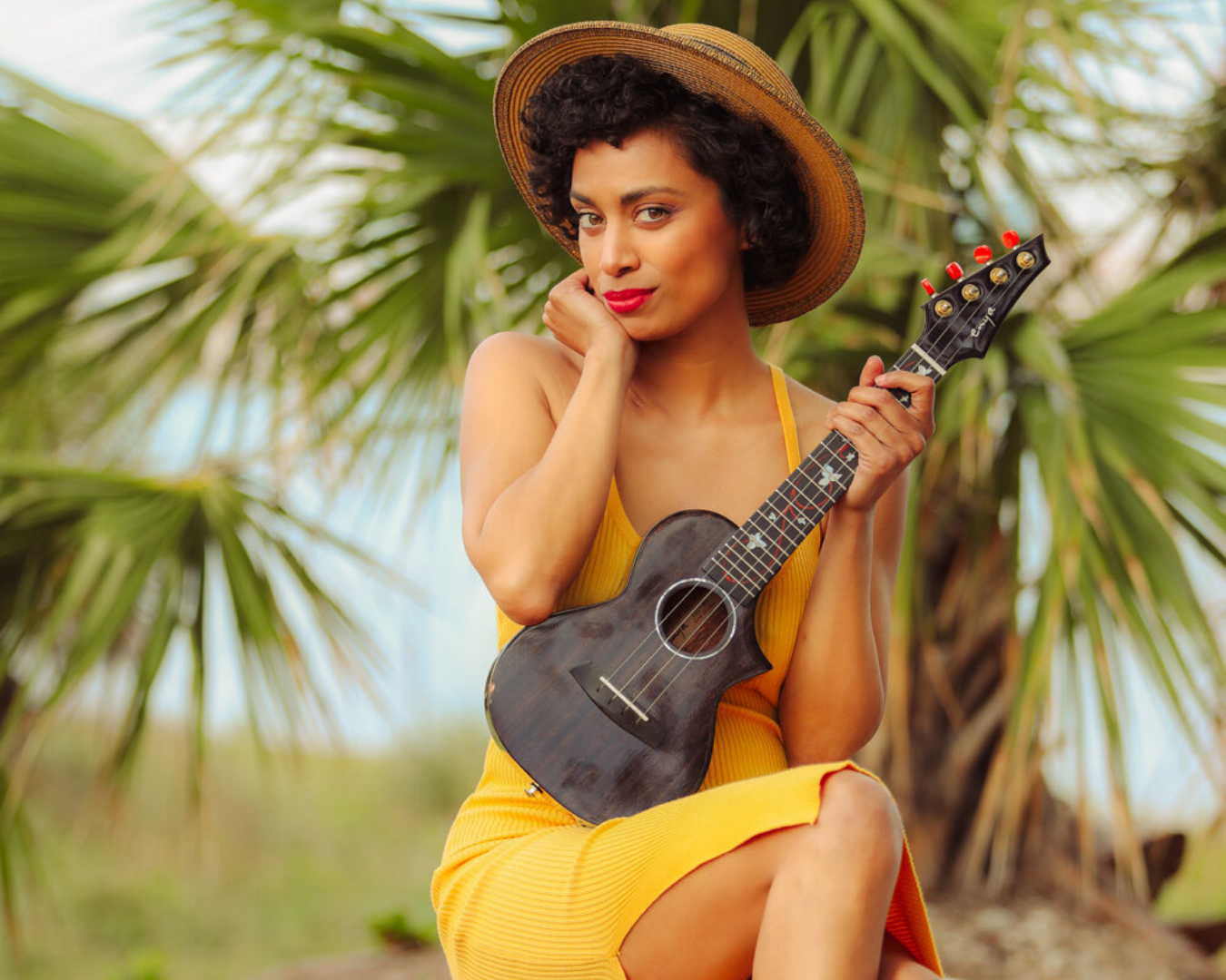 Woman in yellow dress plays ukulele outdoors against tropical palm tree background.