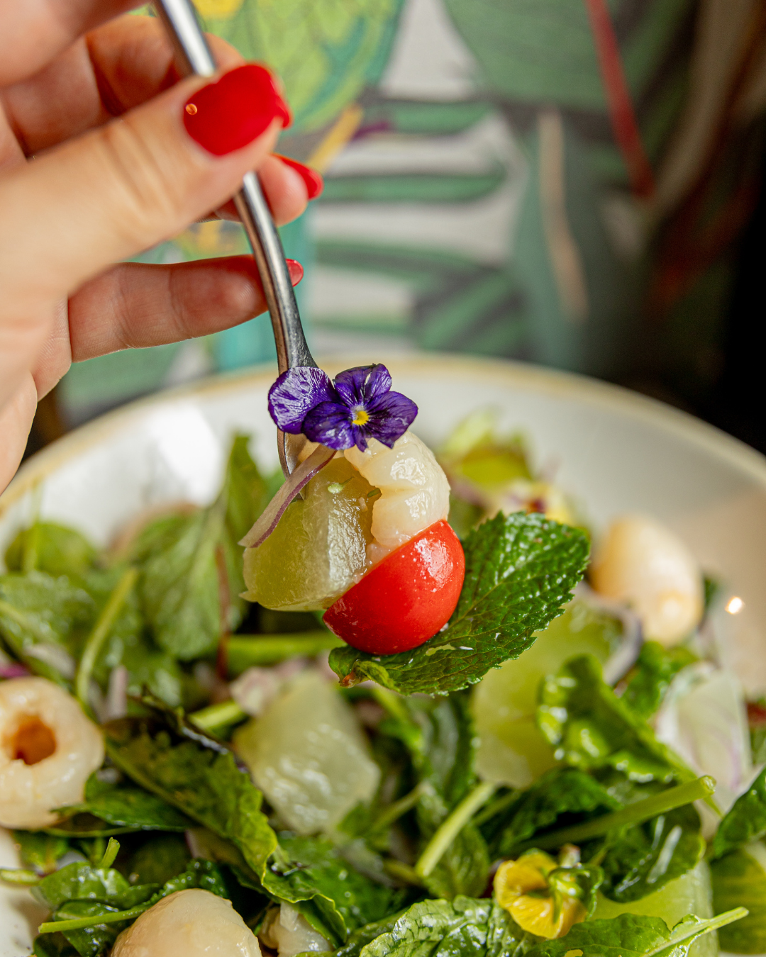 Fresh green salad with cherry tomatoes and herbs being assembled with utensils.