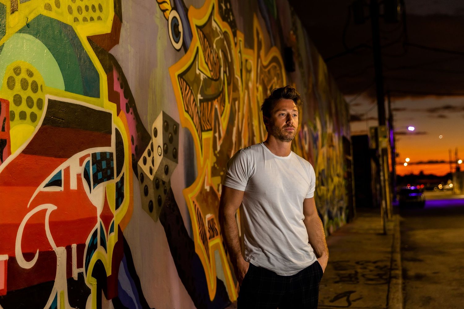 A person stands in front of a vibrant mural with colorful geometric shapes and animal designs in an urban setting.