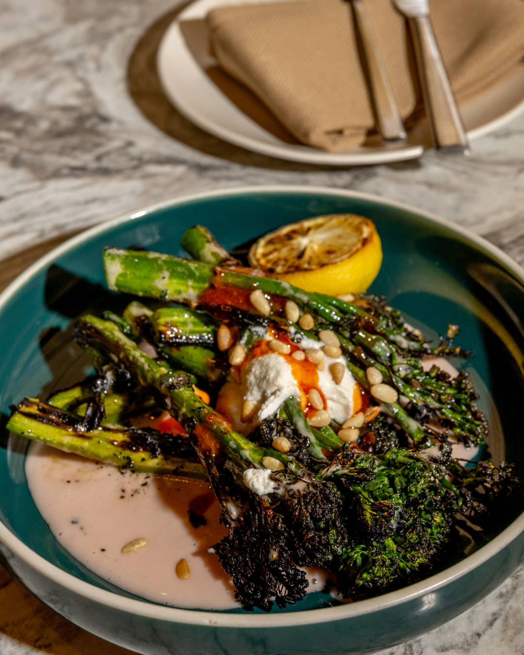 Grilled asparagus and vegetables on a teal plate with sauce and lemon garnish.
