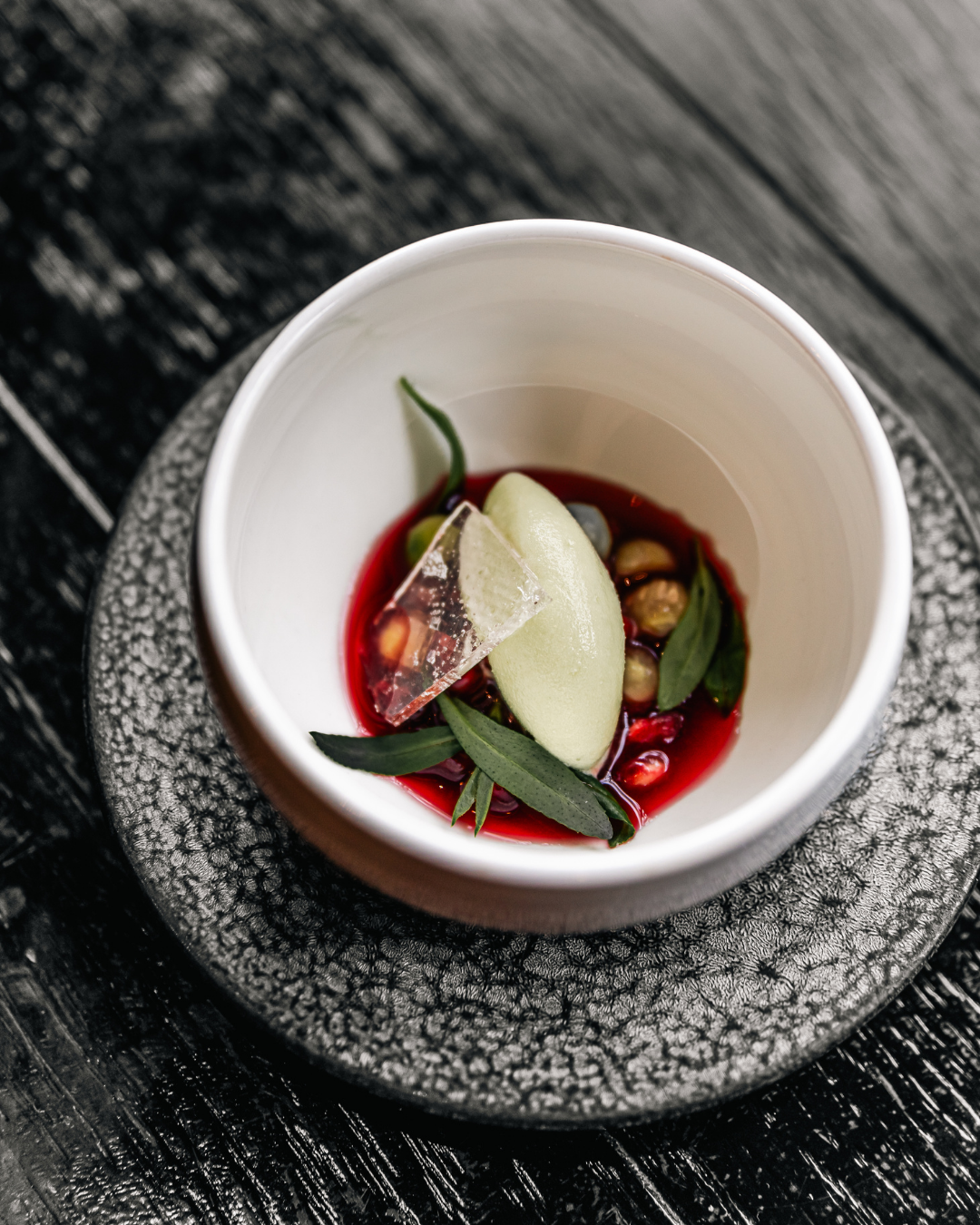 Modern plated dessert with red sauce, green herbs and white cream in an artisanal bowl.