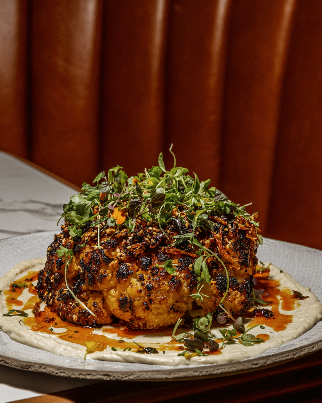 Roasted cauliflower head topped with fresh microgreens and sauce on a white plate.