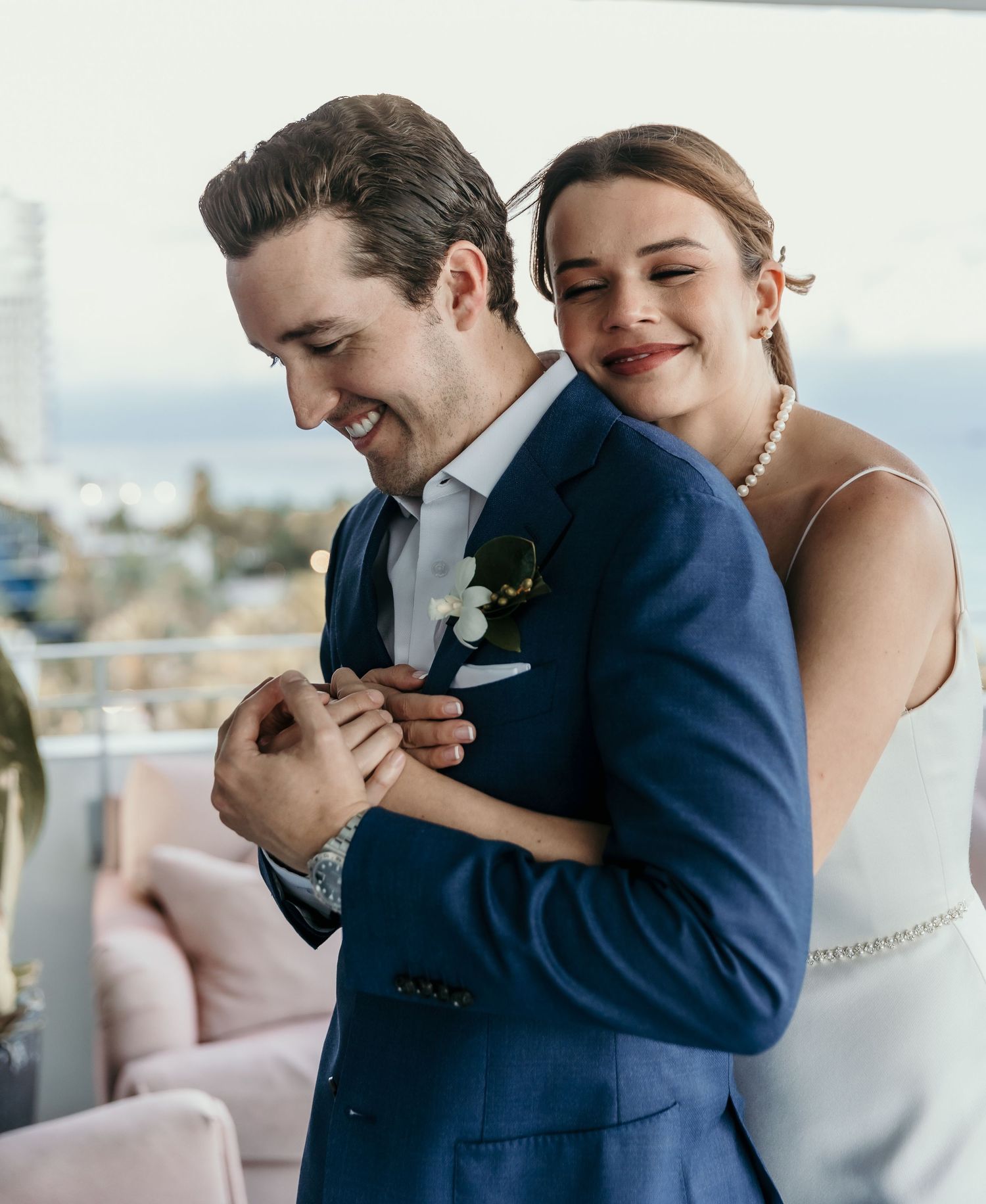 Joyful wedding couple embracing on balcony overlooking city view.