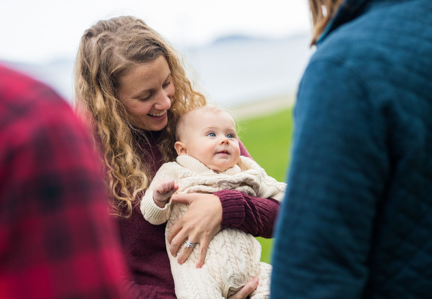 A smiling mother holding her happy baby outdoors in a green field during a family portrait session.