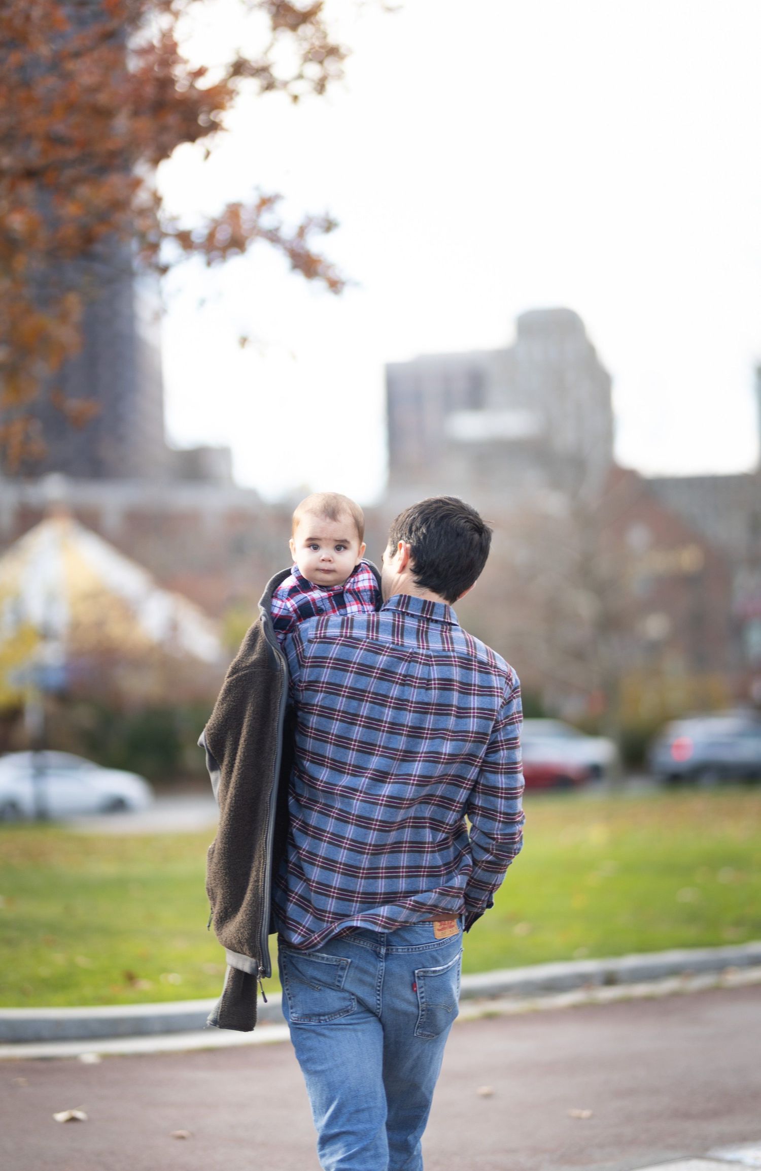 Father carrying his baby on his shoulder while walking through an urban park in autumn.