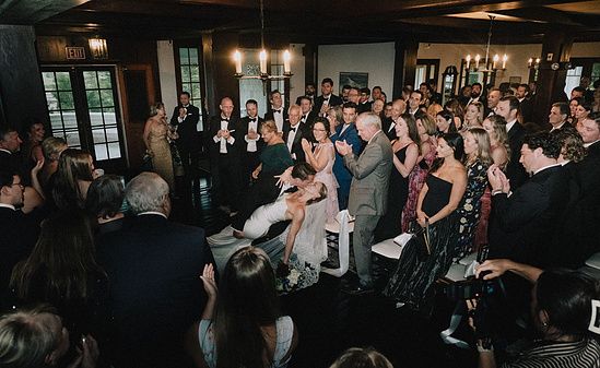 Wedding guests gather and celebrate together during a lively indoor wedding reception ceremony.