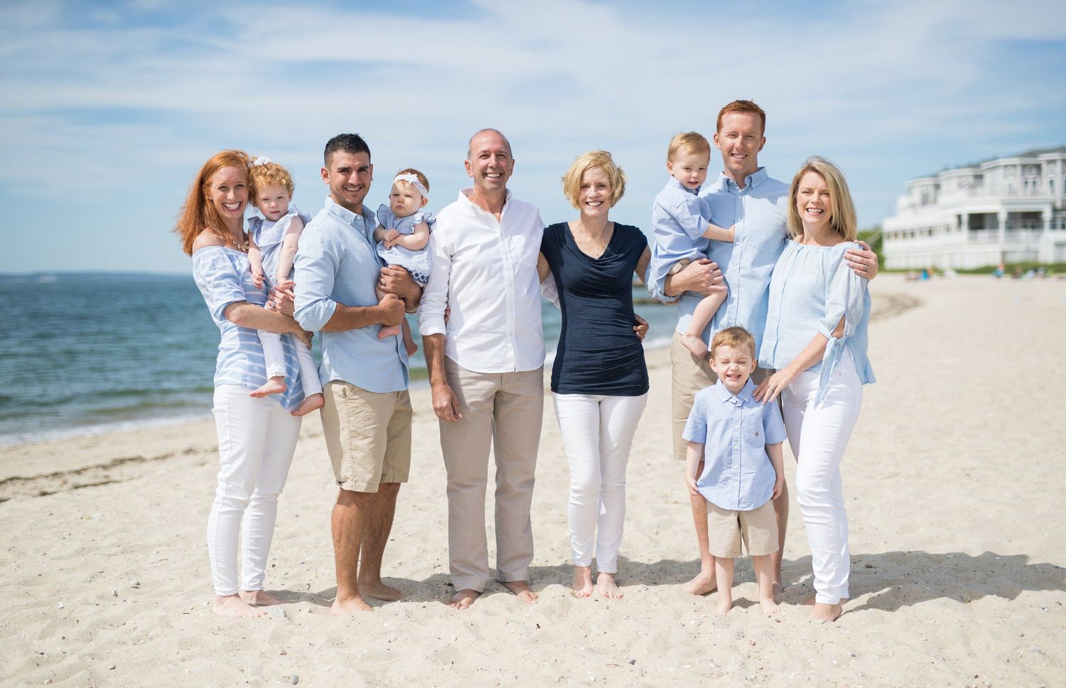 Large extended family posing together on a sunny beach in coordinating blue and white outfits.