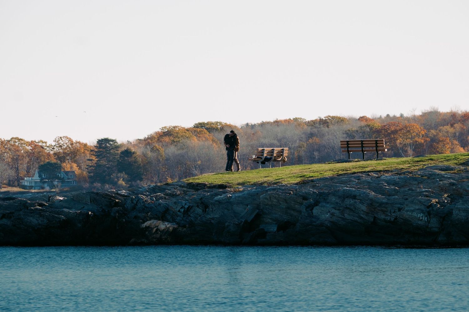 Couple stands on rocky coastal overlook surrounded by fall foliage and calm water.