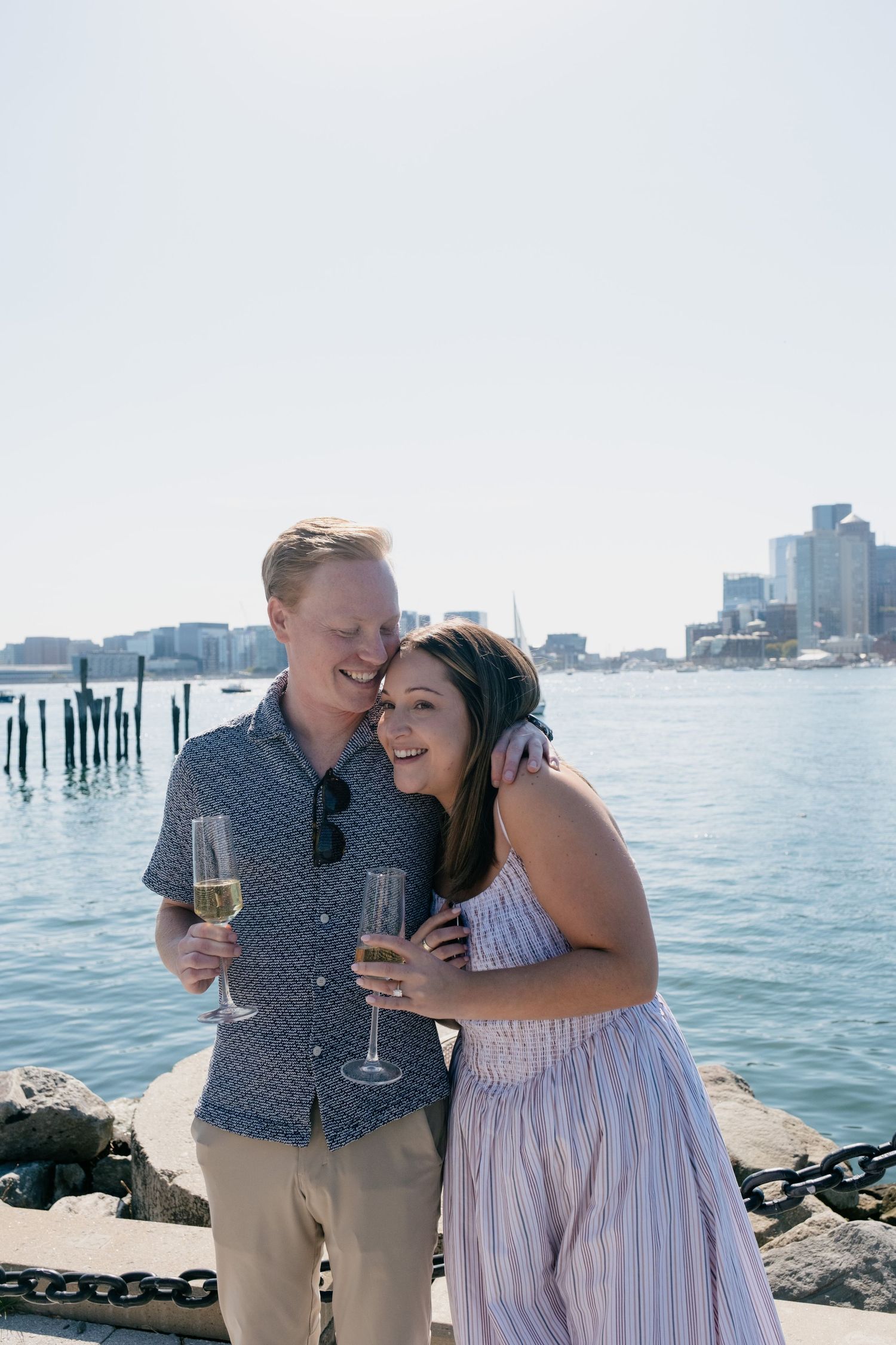 Happy couple celebrating engagement with champagne glasses at Boston harbor waterfront.