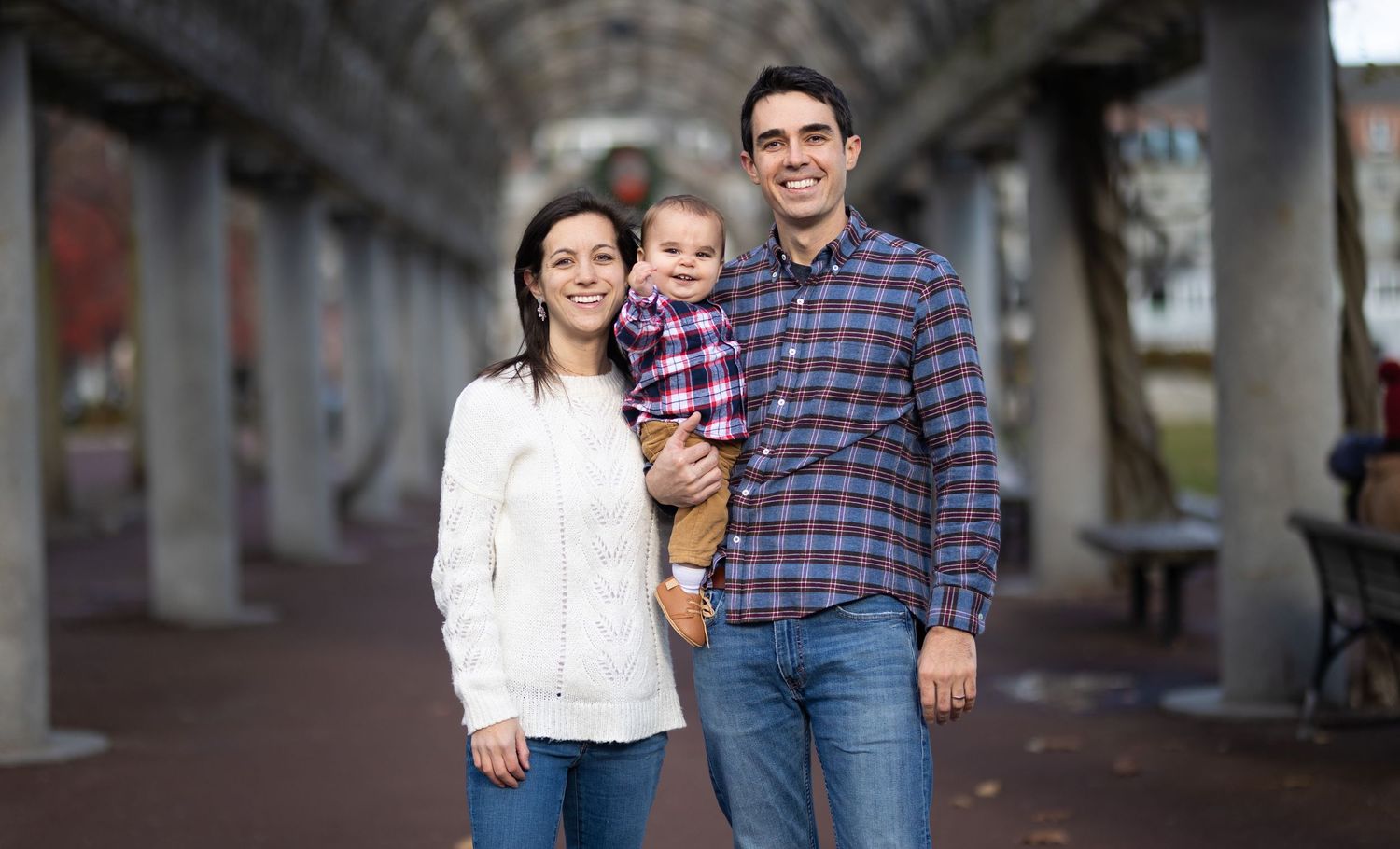 Young family of three smiling together under an arched walkway during an urban family portrait session.