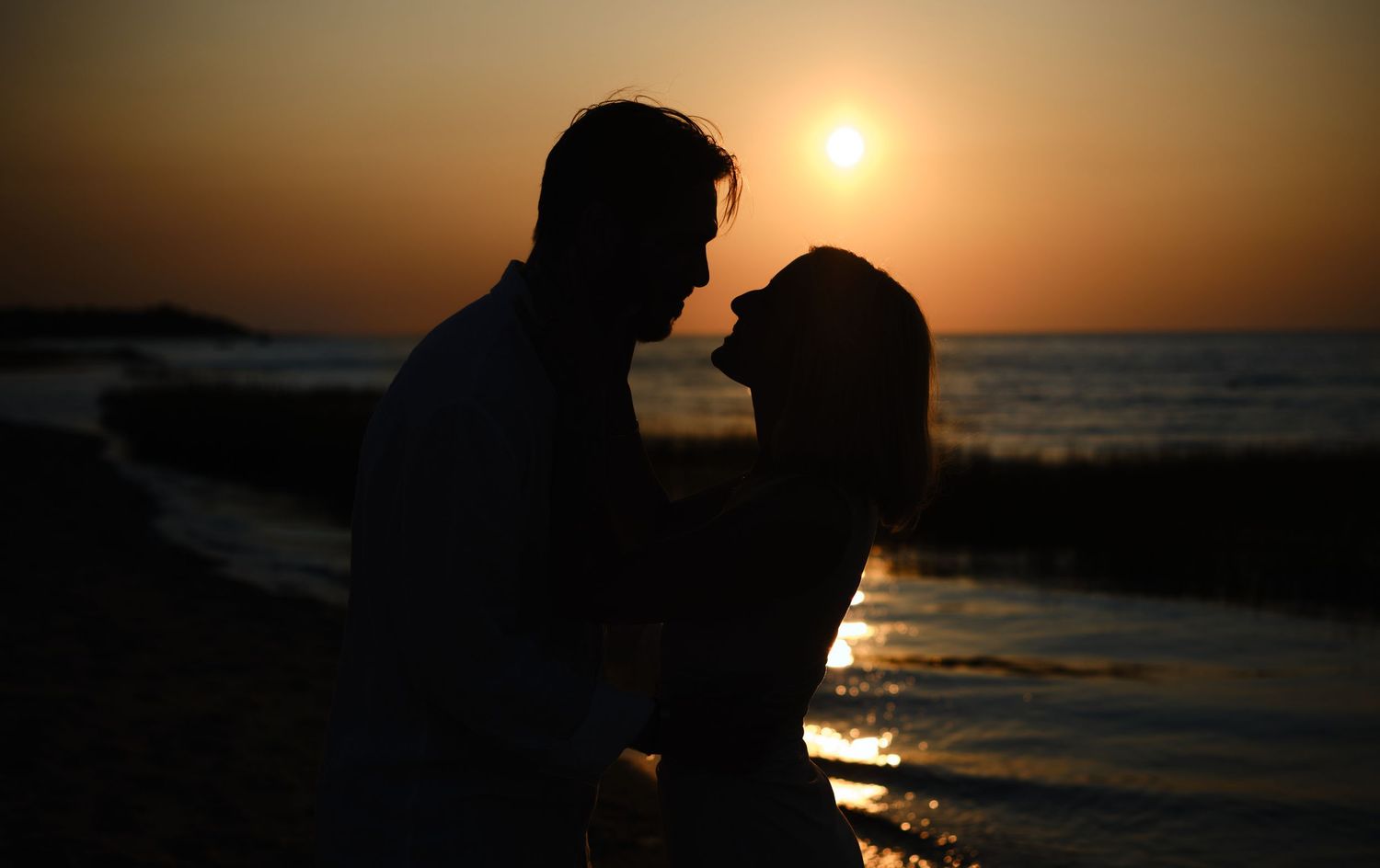 Romantic couple silhouetted against a stunning golden sunset on a peaceful beach.