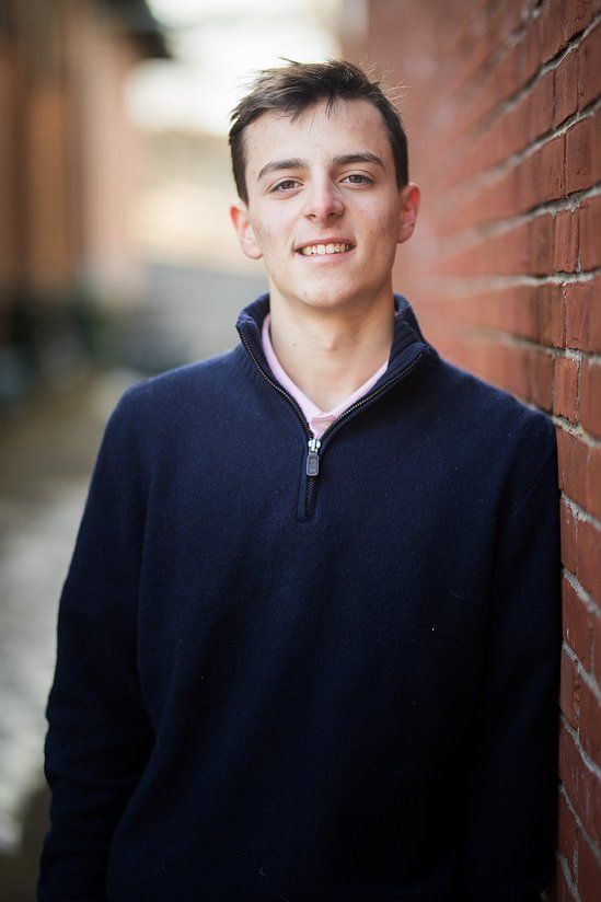 Smiling young man in navy zip sweater leaning against brick wall in urban alley.