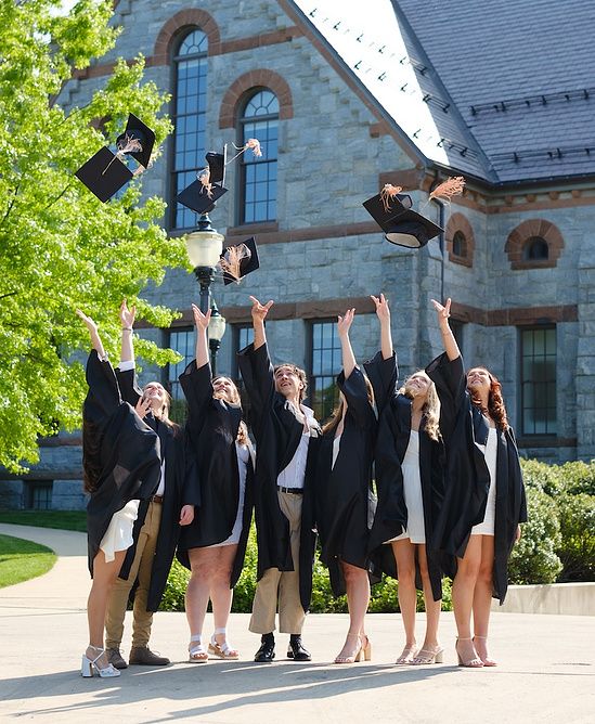 Group of graduates in black robes joyfully tossing caps outside stone university building.