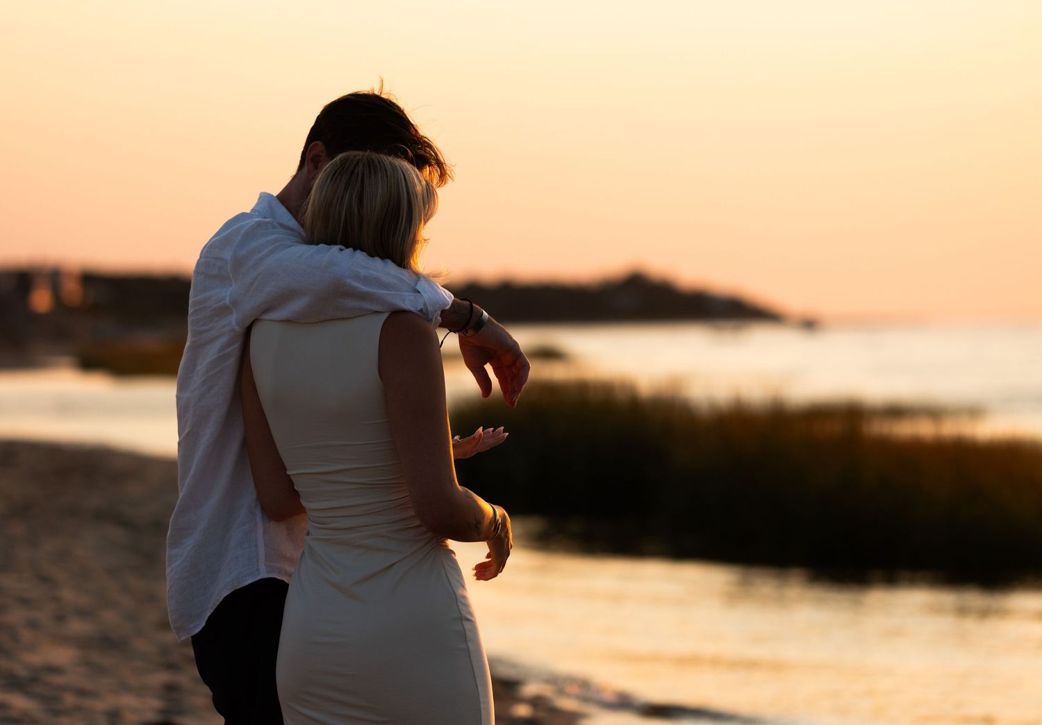 Couple embracing romantically on a serene beach during a warm golden sunset.