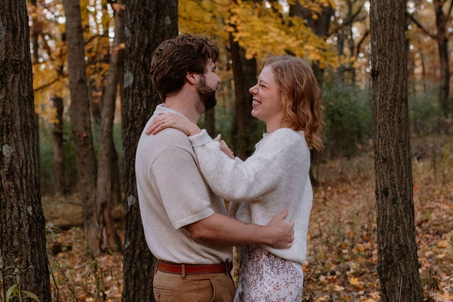 A couple shares a warm embrace while standing among fall trees at sunset during Lapham Peak engagement session