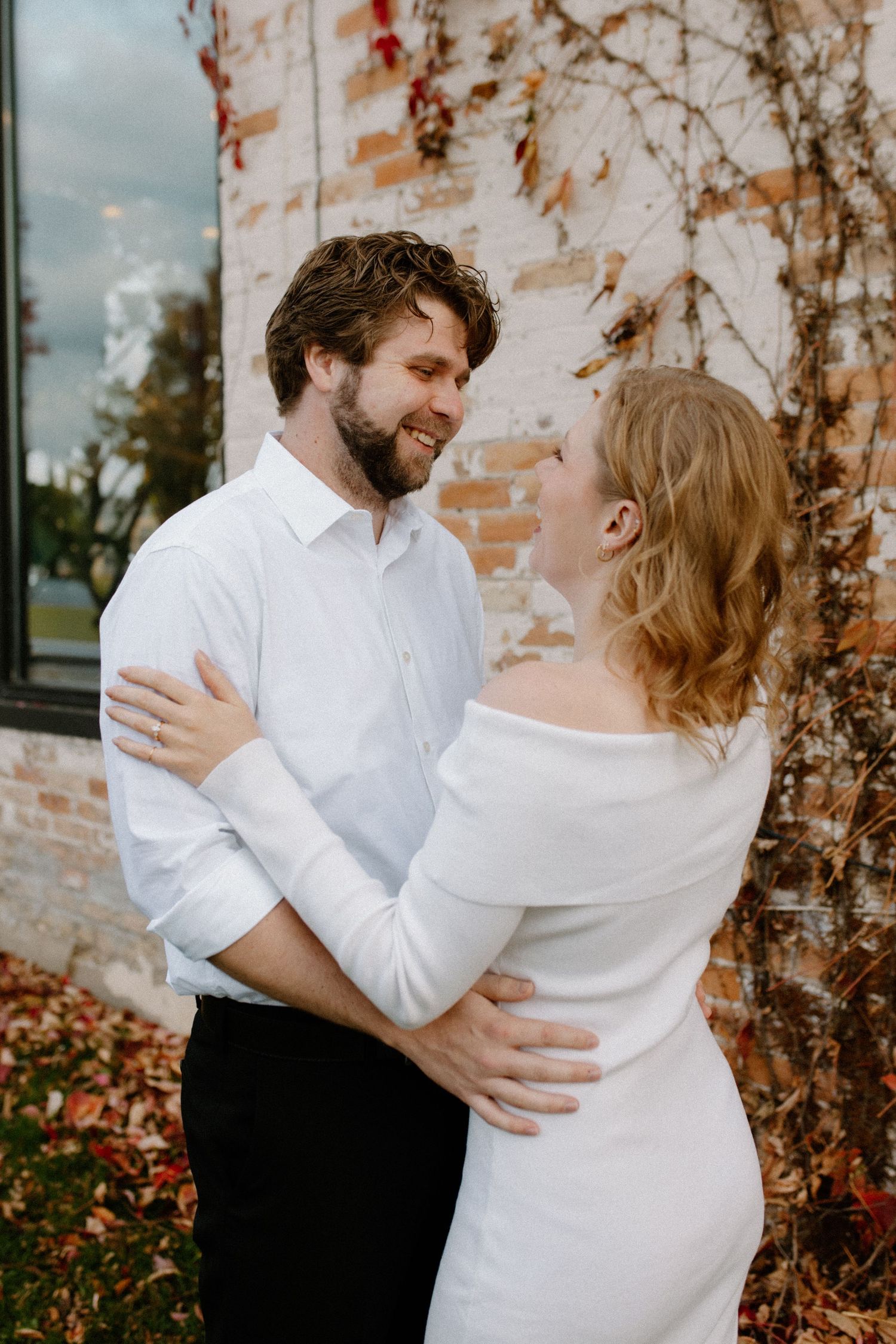 Intimate couples portraits captured against a weathered brick wall with autumn foliage in downtown Oconomowoc engagement session
