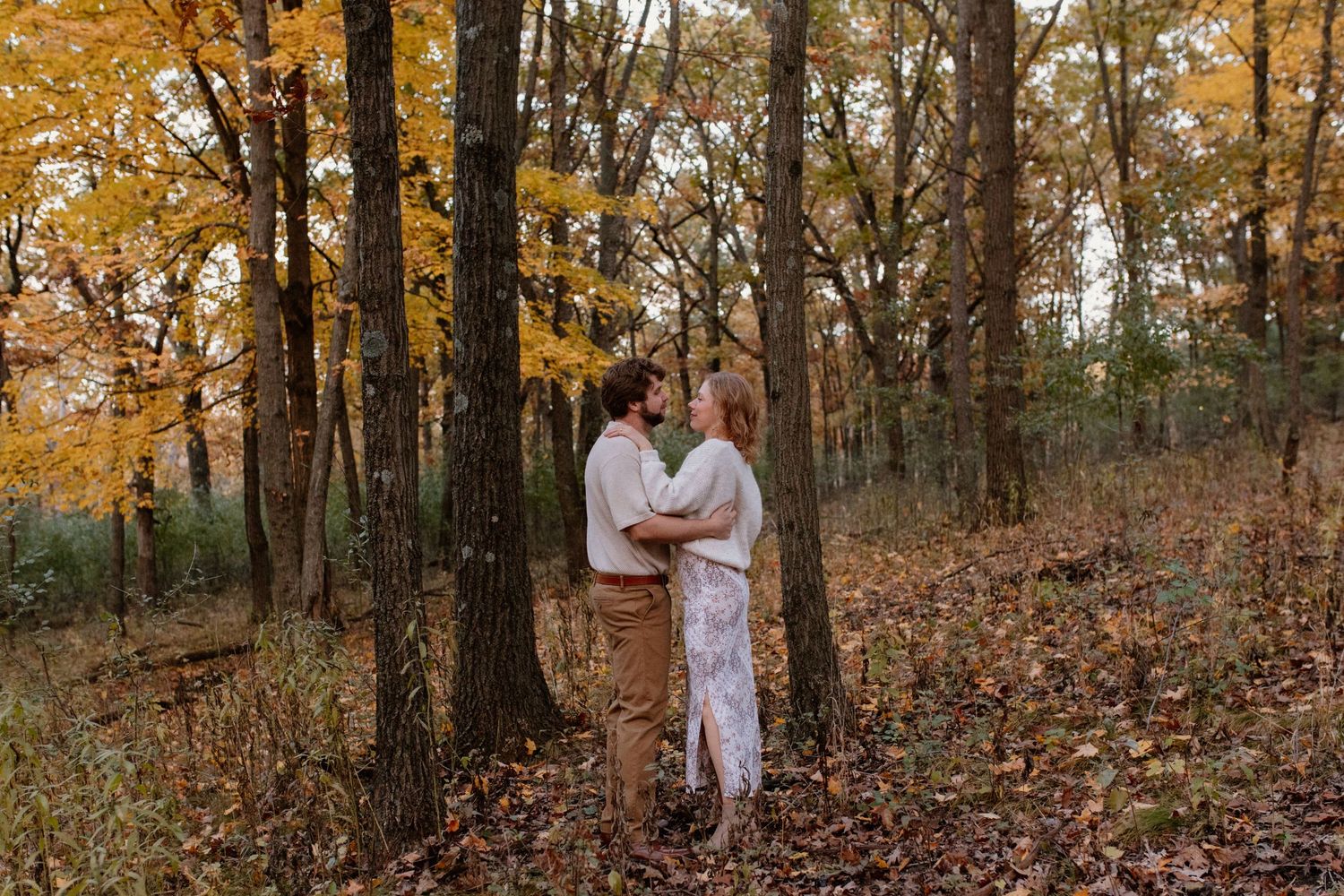 A couple shares an intimate moment among tall trees in autumn light at Lapham Peak engagement session