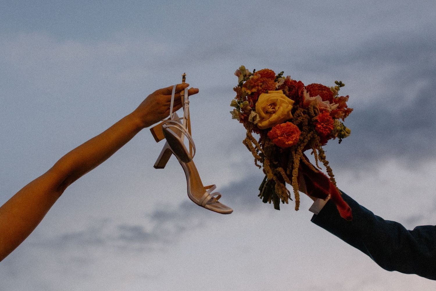 Hands raised holding colorful autumn wedding bouquets against the sky in Madison, WI rooftop golden hour wedding photos