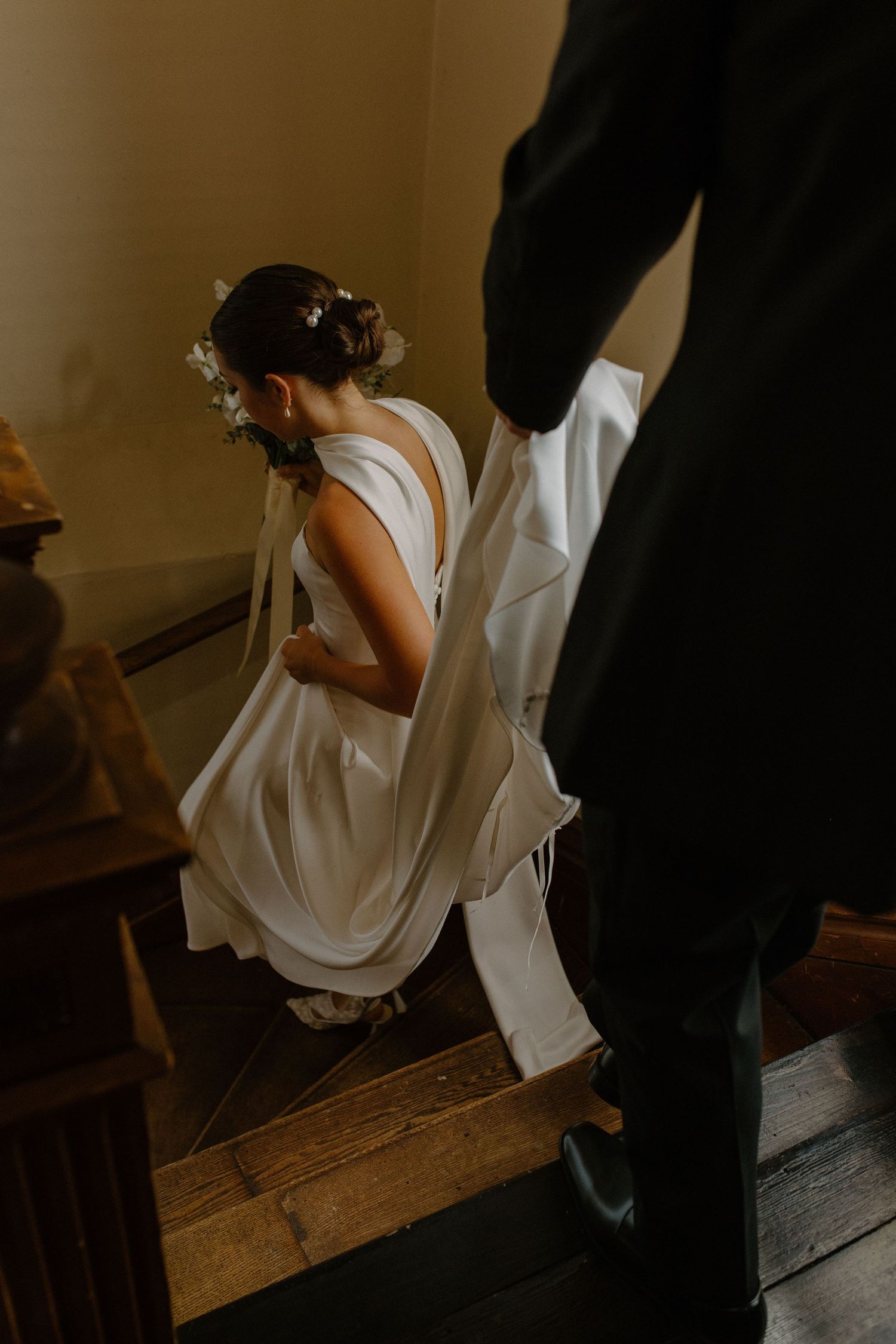 Elegant white wedding dress flowing down wooden stairs in soft lighting during chapel wedding portraits